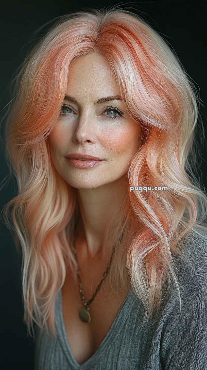 A woman with long, wavy, pastel pink hair wearing a gray top and a necklace.