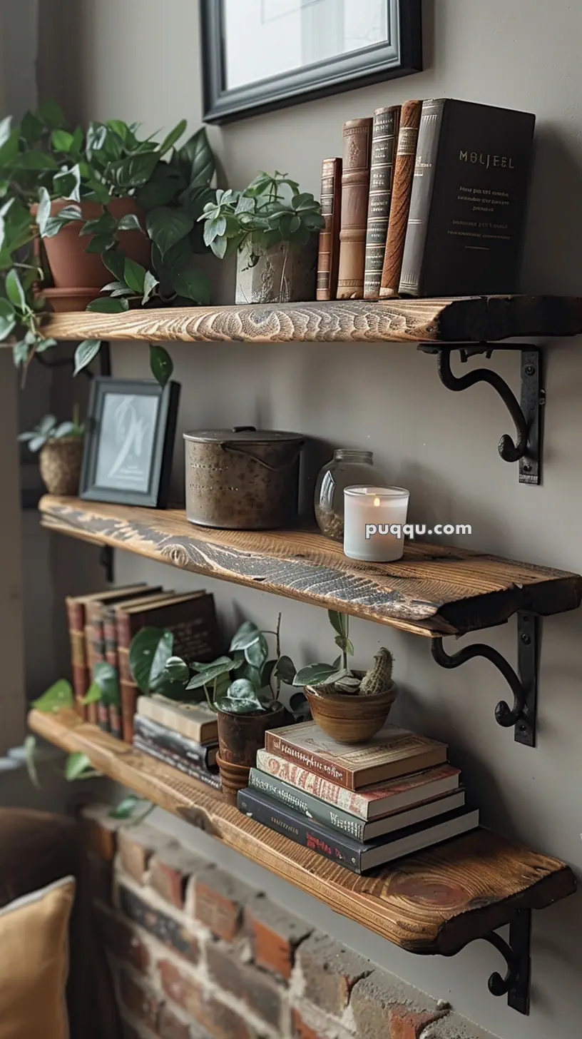 Wooden shelves with books, small potted plants, a framed photo, a metal container, and a lit candle against a brick wall background.