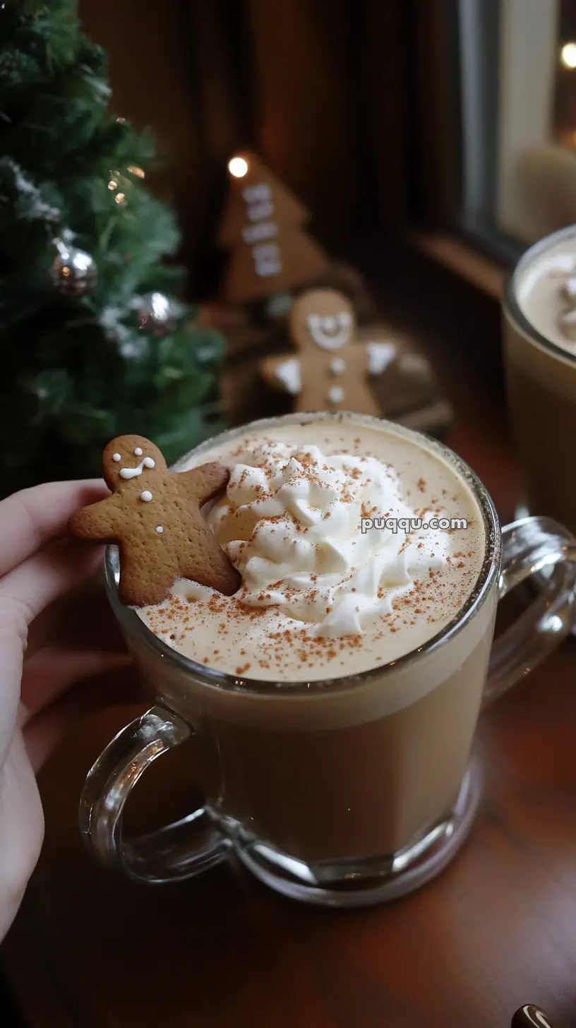 A mug of coffee topped with whipped cream and sprinkled with cinnamon, garnished with a gingerbread cookie, beside a Christmas tree.