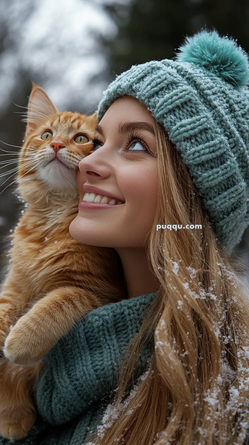 Woman in a snowy setting wearing a knitted hat and scarf, holding an orange tabby cat close to her face.