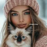 Woman wearing a pink knit hat and scarf holding a fluffy cat with blue eyes.