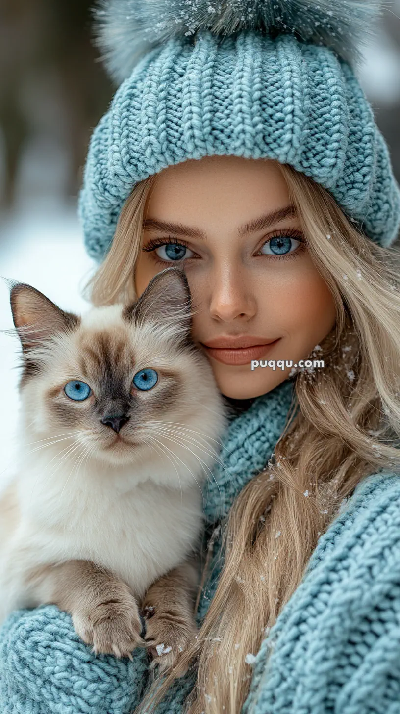 A woman in a blue knit hat holds a cat with similar blue eyes, both looking at the camera in a snowy setting.