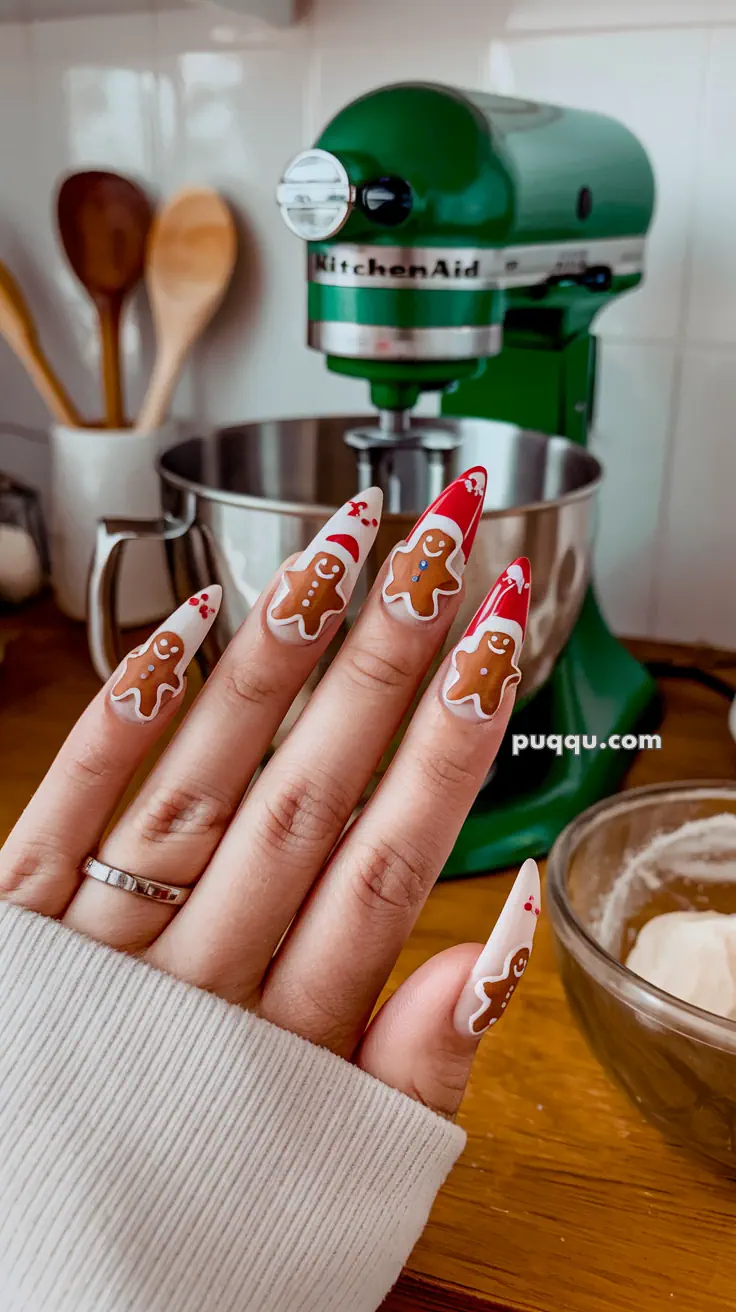 Close-up of a hand with Christmas-themed nail art featuring gingerbread men designs, in front of a green KitchenAid mixer.