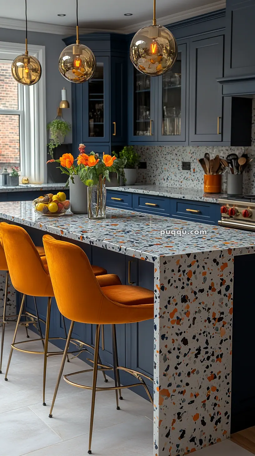 Modern kitchen with navy blue cabinets, terrazzo countertops, orange bar stools, and pendant lights.