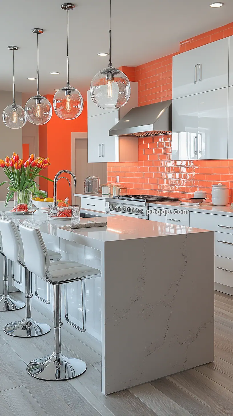 Modern kitchen with orange backsplash, white cabinets, glass pendant lights, and a marble island with white stools.