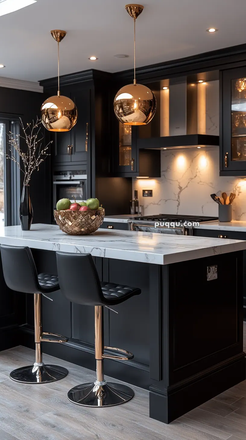 Modern kitchen with black cabinetry, marble countertops, gold pendant lights, two black bar stools, and a fruit bowl on the island.