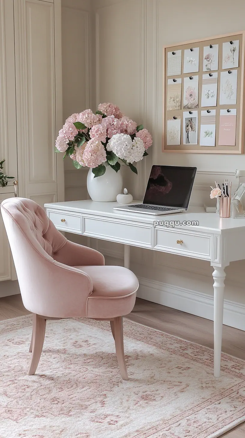 Elegant home office setup with a white desk, pink velvet chair, laptop, vase of hydrangeas, and wall photos.