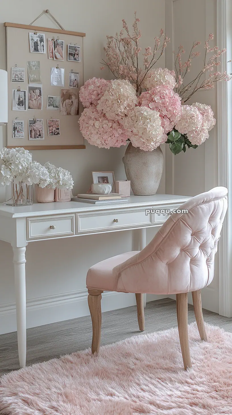 A white desk with a large vase of pink and white hydrangeas, a pink tufted chair, a bulletin board with photos, and a fluffy pink rug.