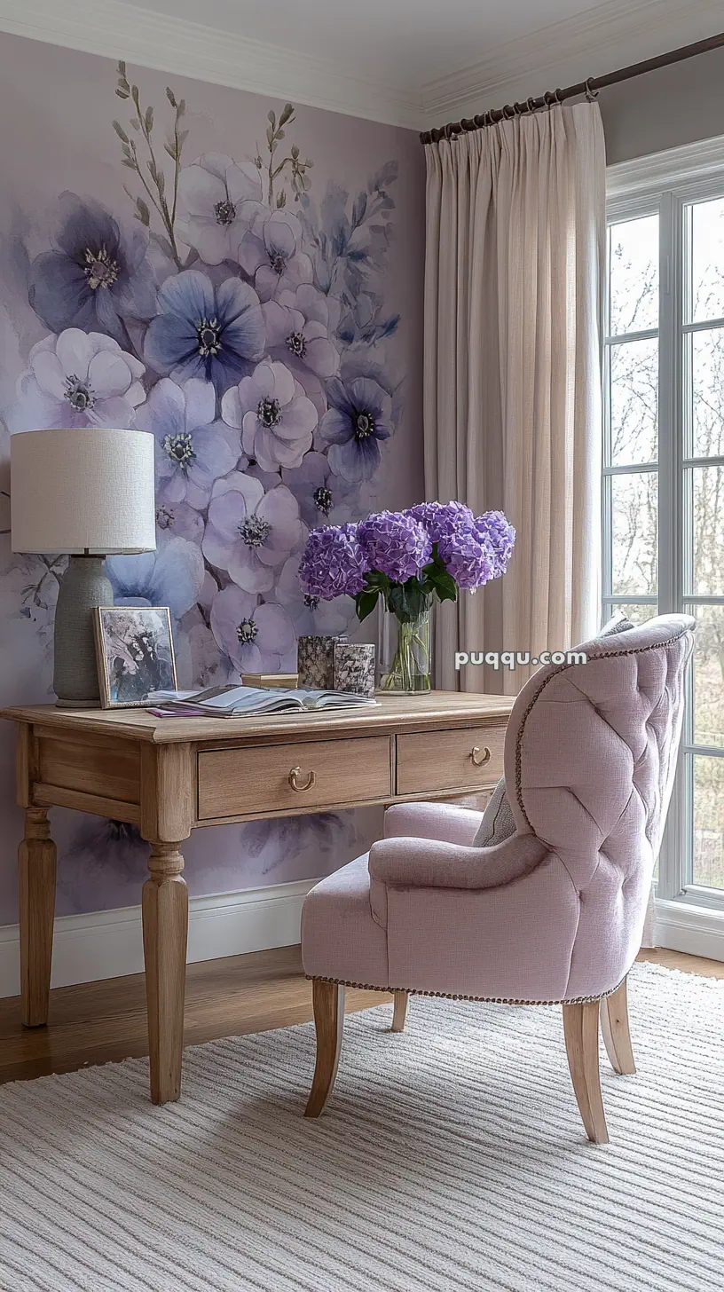 A cozy room with a wooden desk, a light pink upholstered chair, a vase of purple flowers, and a floral mural on the wall.