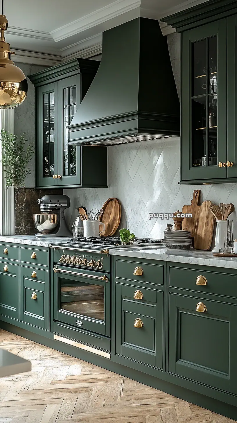 Elegant kitchen with dark green cabinets, brass hardware, and marble countertop; features a gold pendant light and herringbone wood flooring.