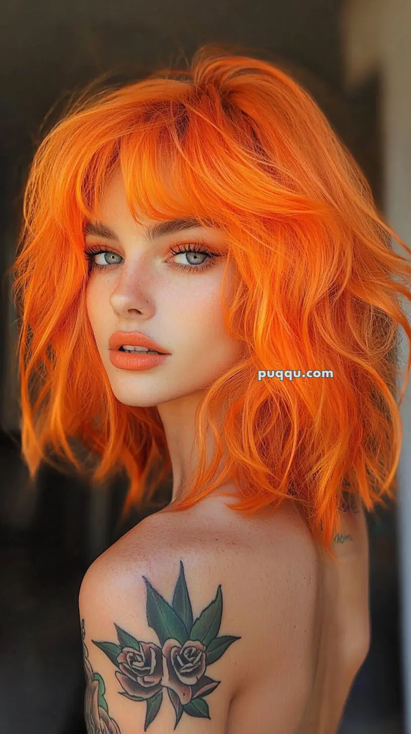 A person with bright orange hair, wearing makeup, and a floral tattoo on their shoulder.