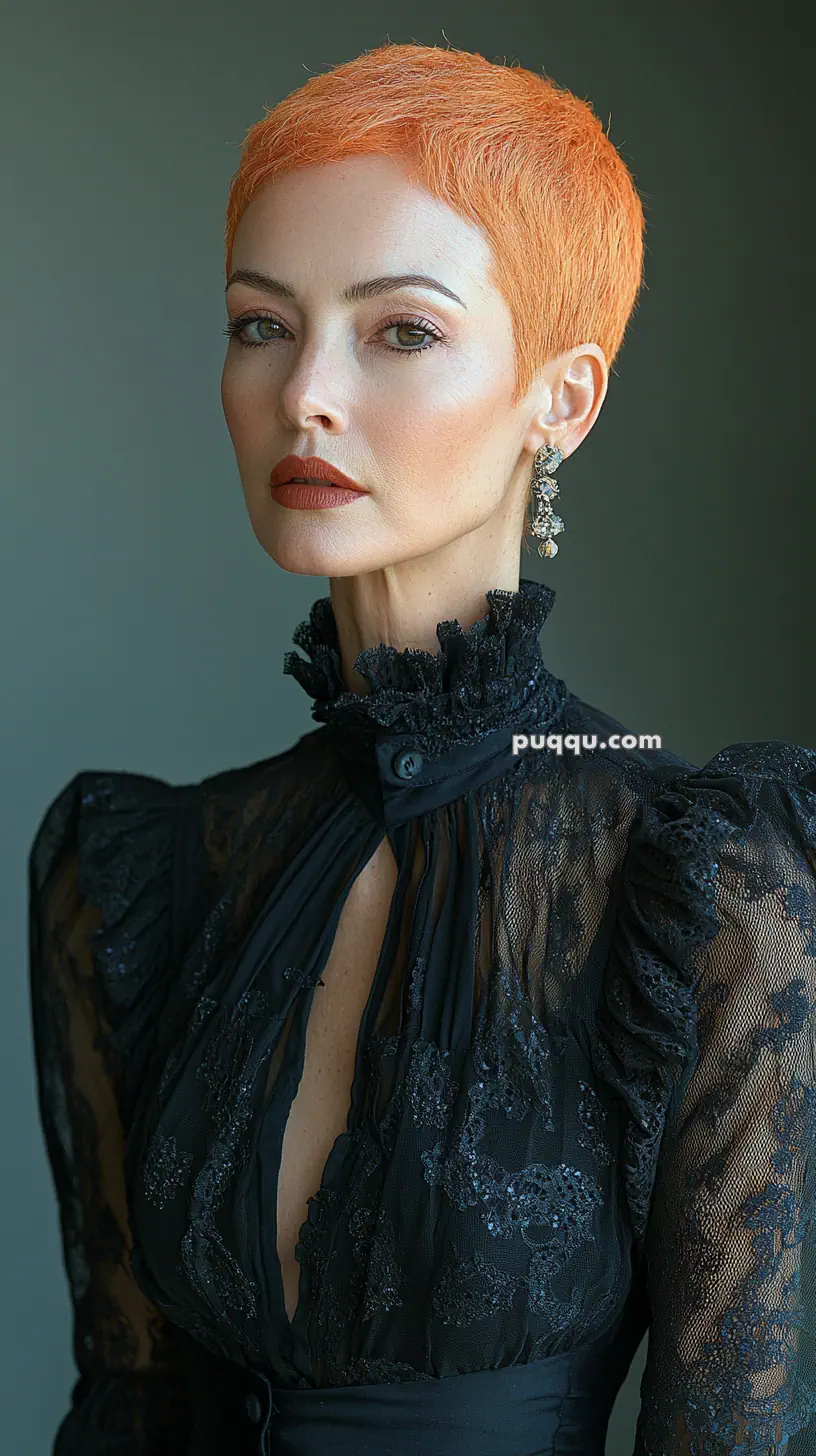 A person with short, bright orange hair wearing a high-necked black lace dress and chandelier earrings.