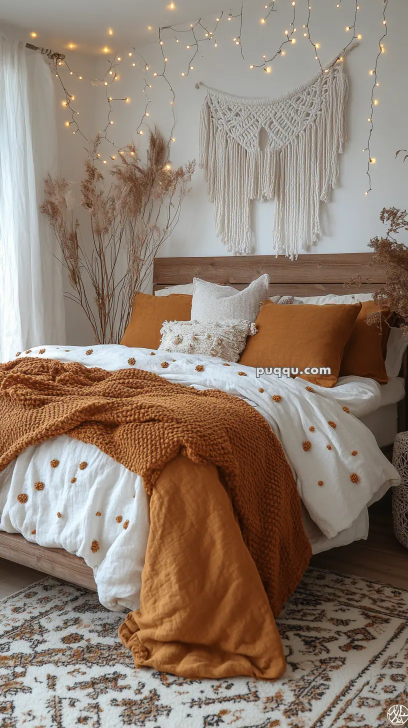 Cozy bedroom with a wooden bed, mustard and white bedding, a macrame wall hanging, fairy lights, and decorative dried plants.