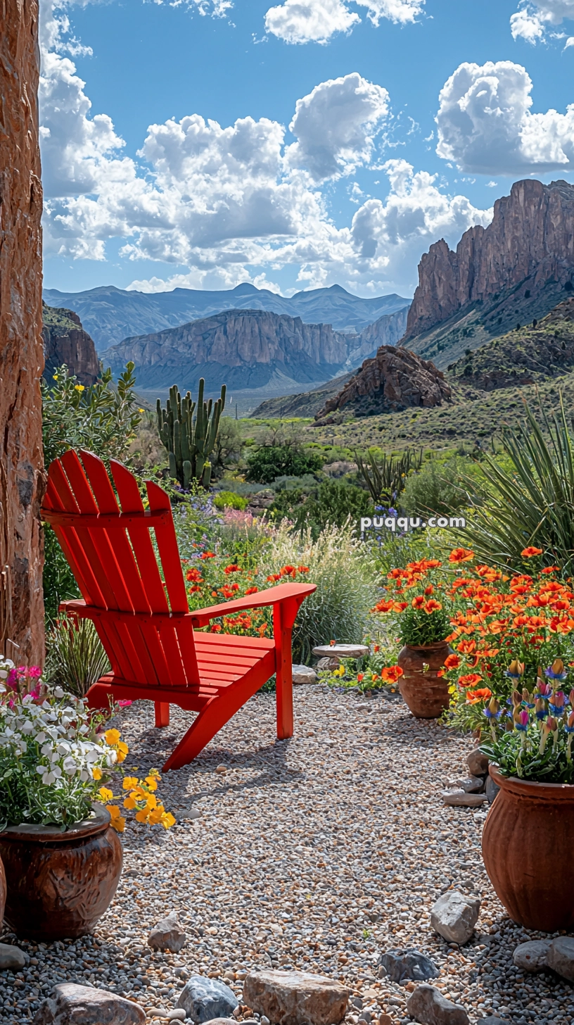 A vibrant red Adirondack chair sits on a gravel patio surrounded by blooming flowers in pots, with a scenic view of distant mountains and a bright blue sky dotted with clouds in the background.