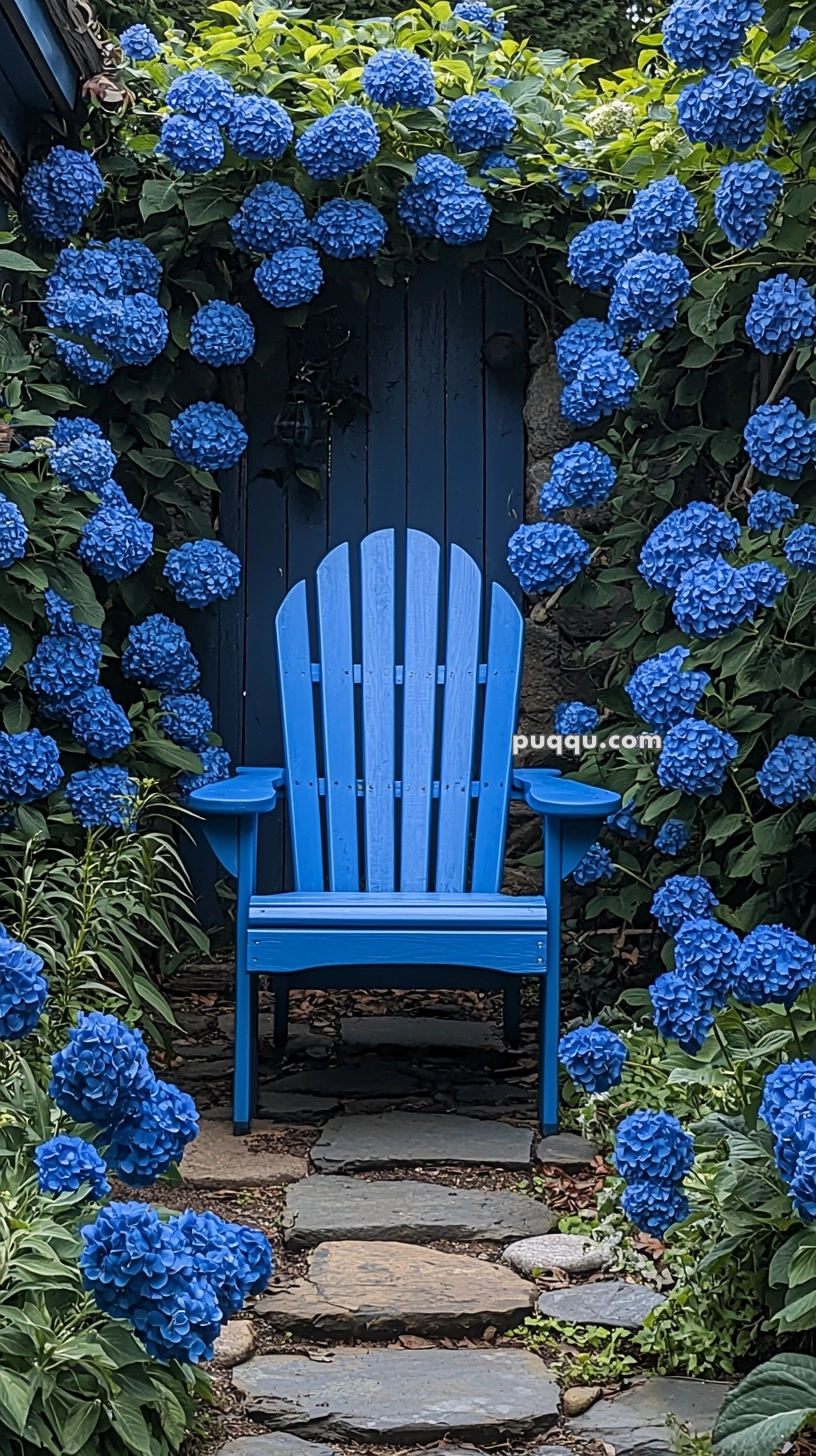 A bright blue Adirondack chair surrounded by lush blue hydrangea blooms next to a stone pathway.