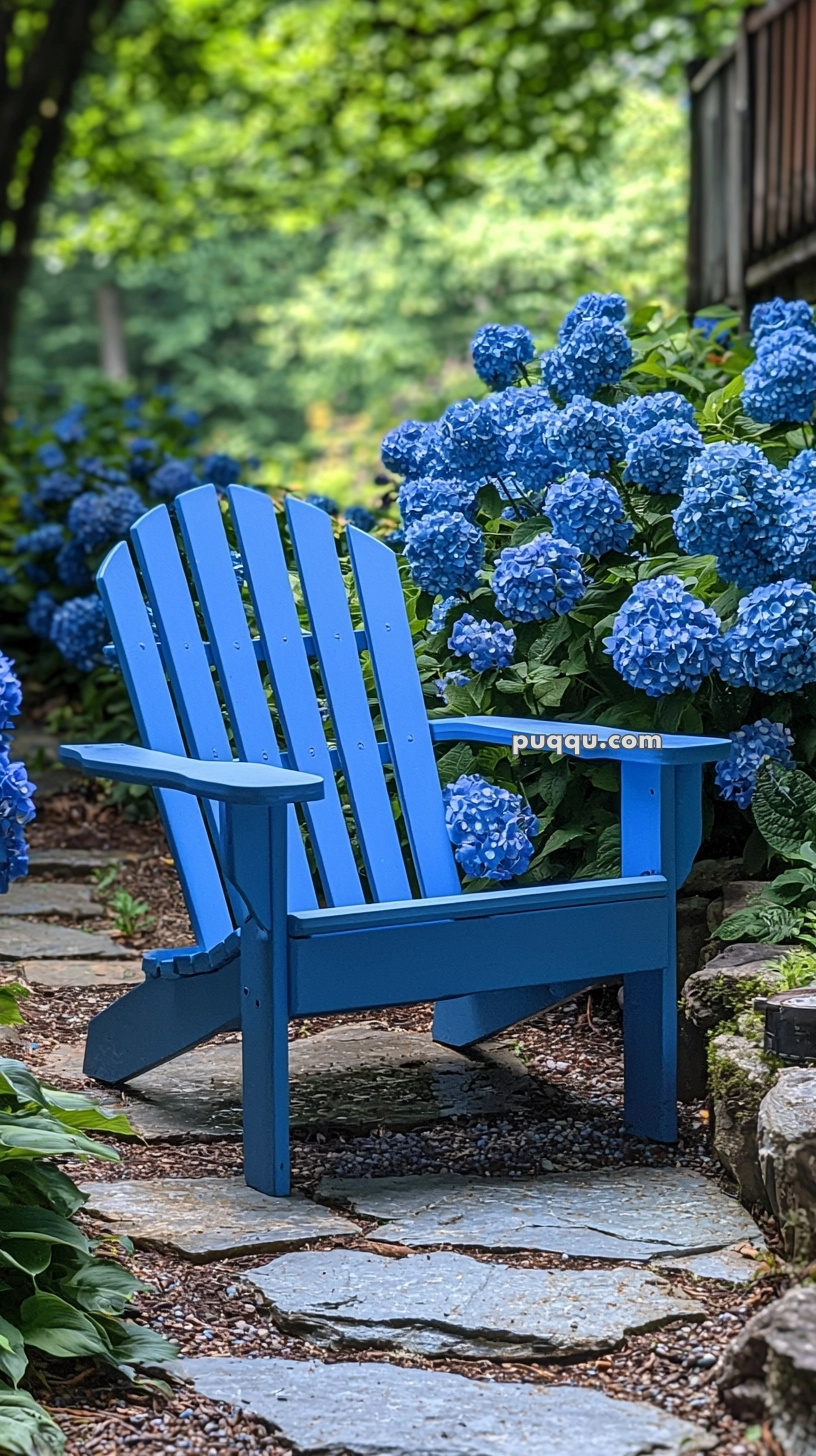A blue Adirondack chair is placed on a stone path surrounded by lush green foliage and vibrant blue hydrangea flowers.
