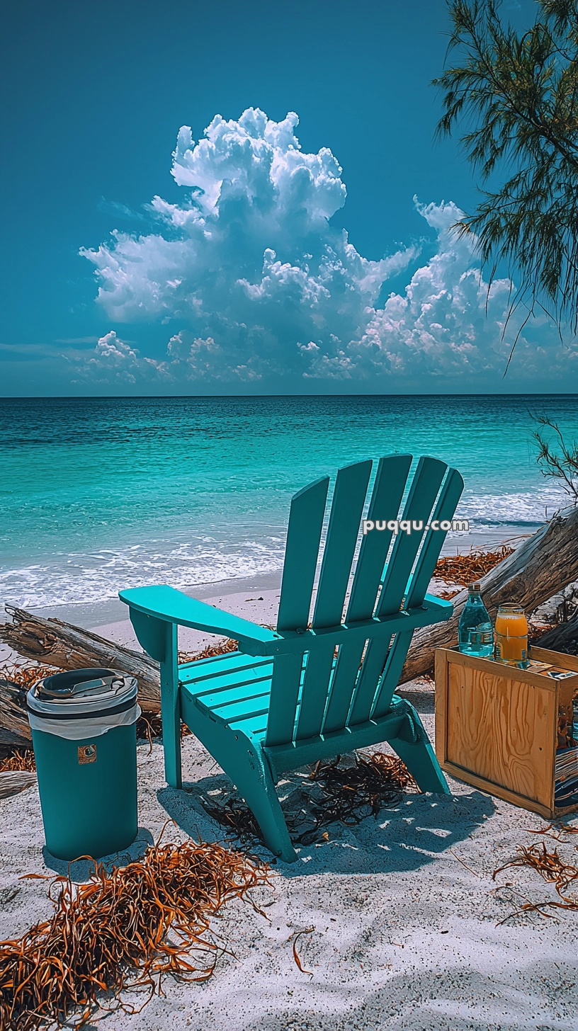 A turquoise Adirondack chair facing the ocean on a sandy beach, next to a small wooden table with drinks and a trash can; a large cloud looms in the vibrant blue sky.