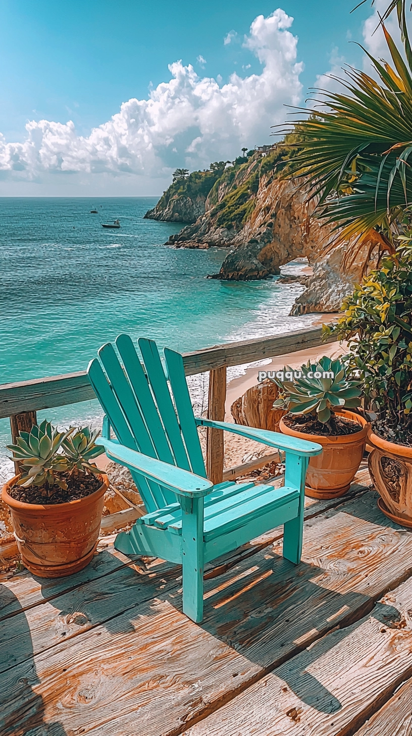 A turquoise wooden chair on a wooden deck overlooking a scenic beach with cliffs and the ocean. Potted plants flank the chair, and a palm tree is partially visible in the foreground. The sky is blue with scattered clouds.