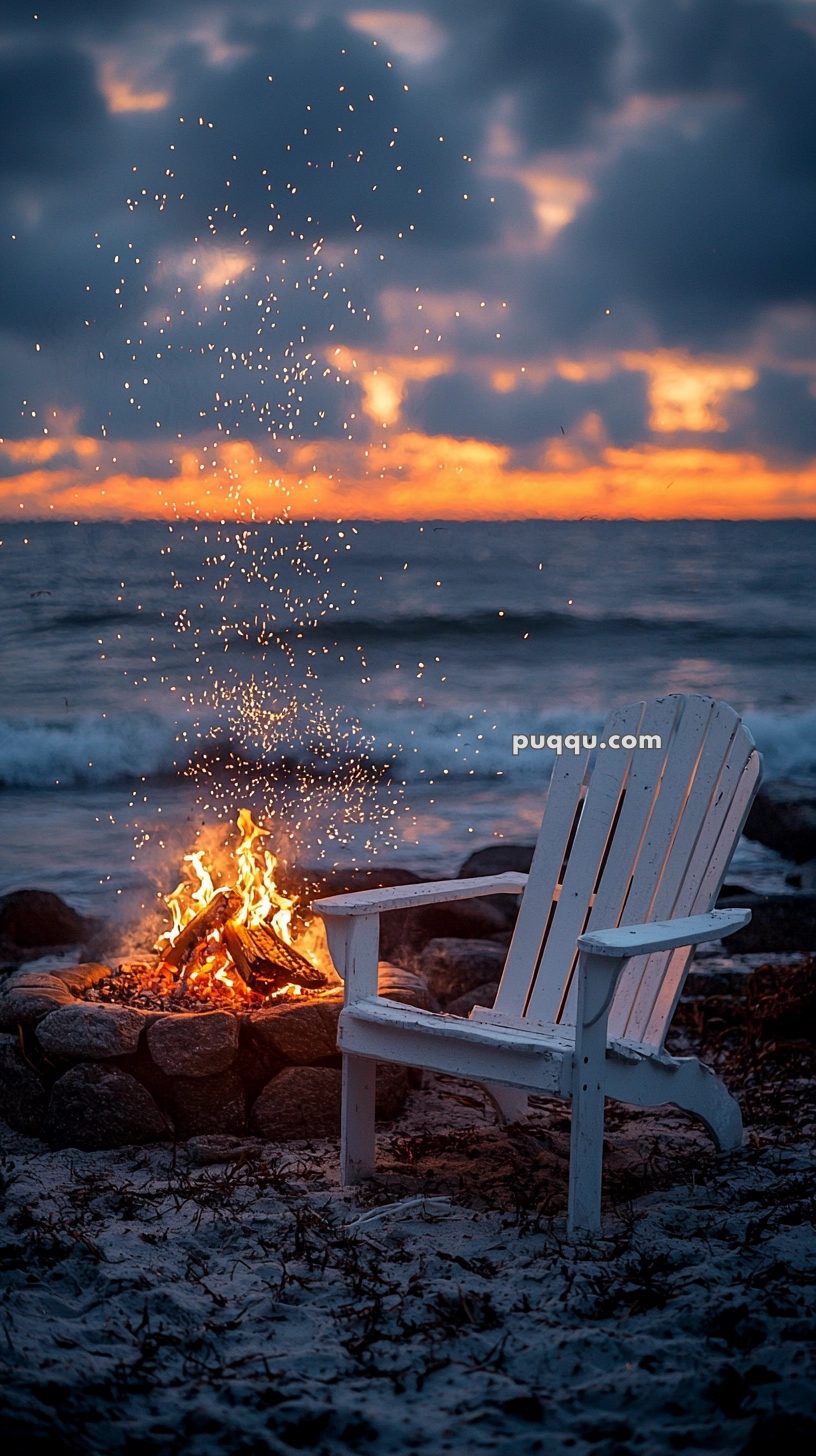 A white Adirondack chair next to a campfire on a sandy beach during sunset, with ocean waves in the background and glowing embers rising into the sky.
