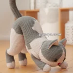 Crocheted cat toy with gray and white stripes, positioned playfully on a wooden floor in a room with blurred background decor.