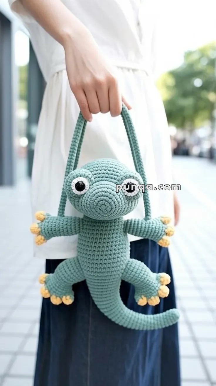 A person holding a crocheted green lizard-shaped purse with large eyes and yellow toes, suspended from its long straps.