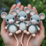 Three crocheted mice with gray bodies, pink noses, and long tails are held in two hands outdoors, with blurred greenery in the background.