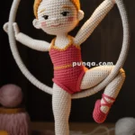 A crocheted doll designed as an acrobat, dressed in a red outfit, posed gracefully on a circular hoop, with a bun hairstyle and ballet shoes, all crafted from yarn.