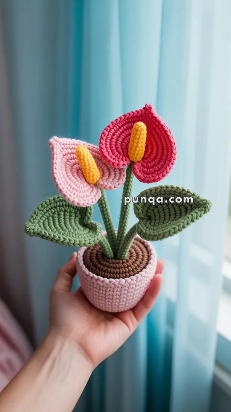 A crochet calla lily plant with pink and red petals and yellow spadices, held in a hand in front of a blue curtain.