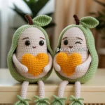 Two crocheted avocado dolls sitting next to each other on a bench, each holding an orange heart. They have green outer layers with leaves on top and are smiling, with one winking.