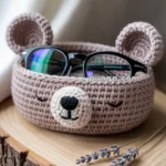 Crocheted bear-shaped basket holding a pair of glasses, placed on a wooden surface with sprigs of lavender nearby.