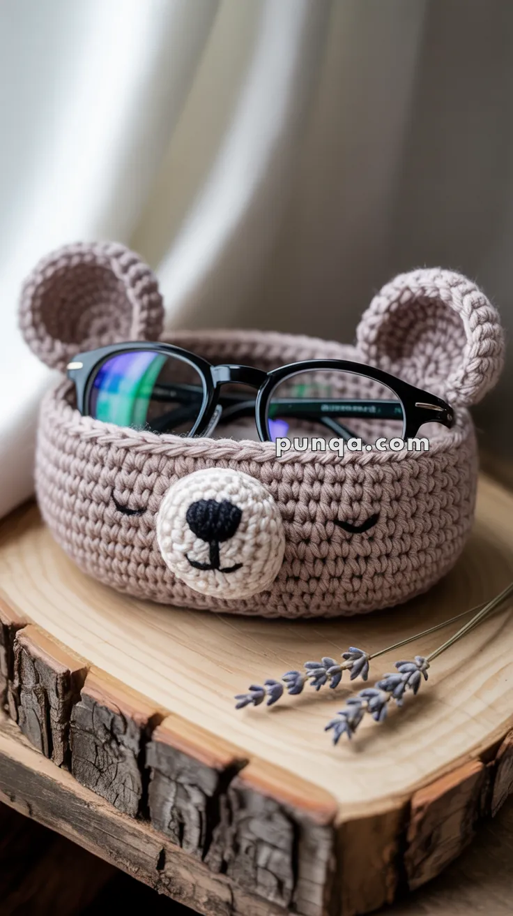 Crocheted bear-shaped basket holding a pair of glasses, placed on a wooden surface with sprigs of lavender nearby.
