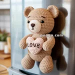 A crocheted teddy bear magnet attached to a refrigerator, holding a pink heart with the word 'LOVE' stitched on it.