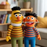 Two crocheted dolls in colorful striped outfits standing on a wooden table in a cozy living room setting with a bookshelf and potted plant in the background.