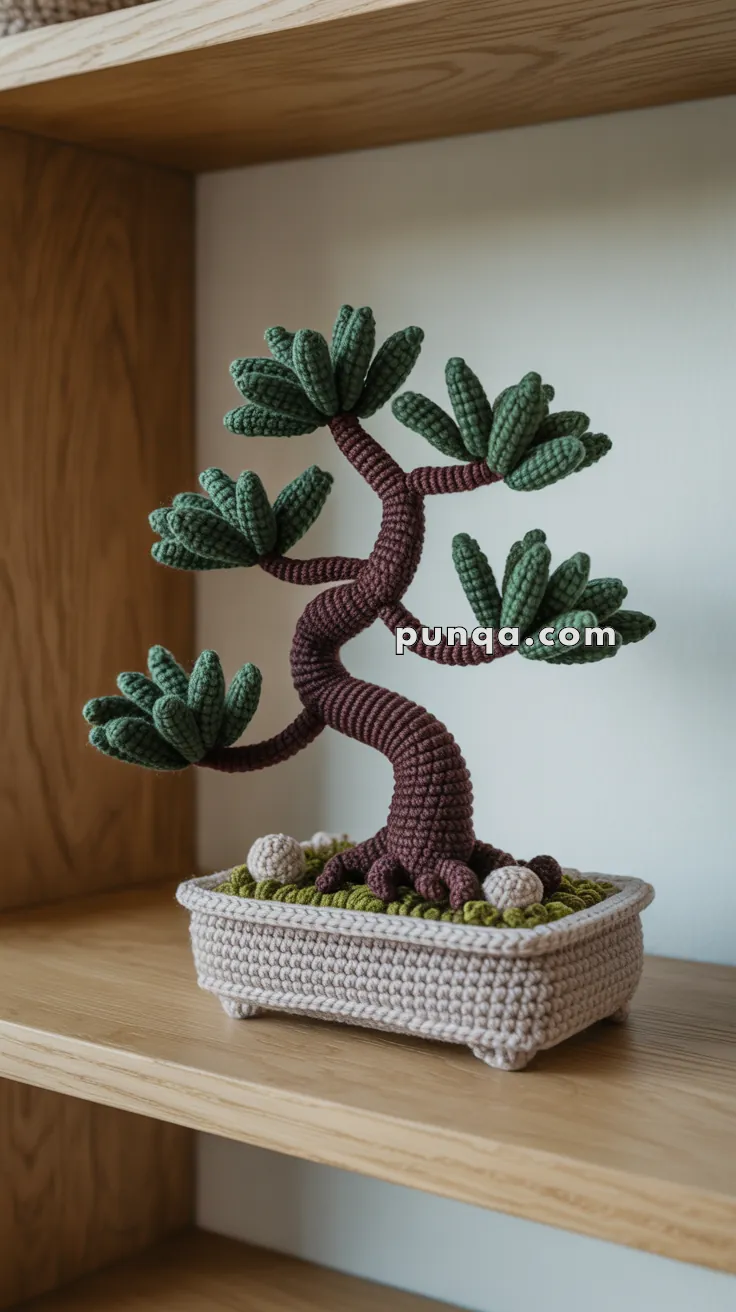A crocheted bonsai tree with green leaves and a brown trunk, placed in a knitted planter on a wooden shelf.