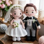 Crocheted bride and groom dolls dressed in wedding attire, with the bride holding a bouquet, placed on a wooden surface alongside a sign that reads 'happily ever after.'