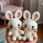 Two crocheted white bunny dolls with large ears held in hands, with a cozy room setting in the background.
