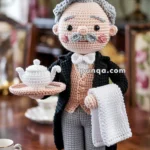 A crocheted butler doll of an elderly man with gray hair and a mustache, dressed in a formal suit with a vest, holding a tray with a teapot and a white cloth, standing on a wooden table with tea cups around it.