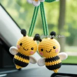 Car interior showing two crocheted bee ornaments hanging from a rearview mirror, with a crocheted white and yellow flower above them.