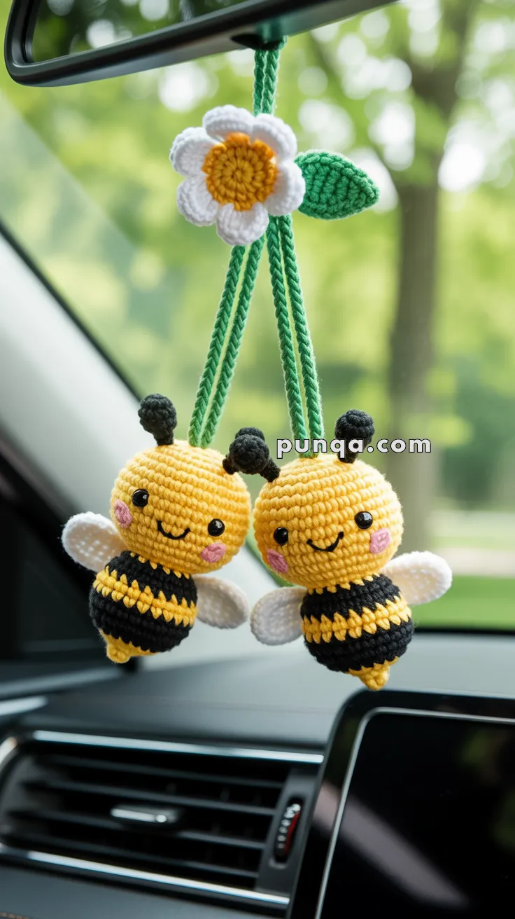 Car interior showing two crocheted bee ornaments hanging from a rearview mirror, with a crocheted white and yellow flower above them.
