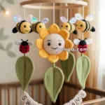 A wooden crib mobile featuring crocheted bees, ladybugs, and a smiling sunflower, with green leaves hanging down, above a crib adorned with the words "Sweet Dreams" in crocheted letters.