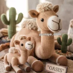 A knitted camel toy with a smaller camel in front, surrounded by knitted cacti, and a sign reading "OASIS" on a sandy surface.