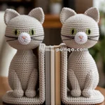Two crocheted cat-shaped bookends holding three books on a wooden table, with a blurred background.