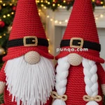 Two crocheted gnome figures with long white beards and red hats stand in front of a Christmas tree and candles, creating a festive atmosphere.