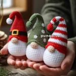 A person holding three crocheted gnomes with hats, in shades of red and green, on a wooden surface near pinecones.