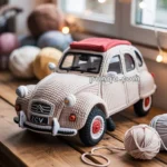 A crocheted model of a vintage car, resembling a Citroën 2CV, is placed on a wooden table surrounded by balls of yarn. The car features detailed stitching with a red roof and is set against a softly lit background with fairy lights.