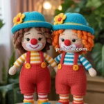 Two crocheted clown dolls wearing blue hats with yellow flowers, red overalls, and colorful striped shirts, standing on a wooden surface in a warmly lit room.