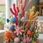 A colorful crocheted underwater scene featuring various sea creatures like an octopus, fish, and starfish among coral and sea plants, displayed on a wooden stool in a room with a window.