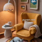 A cozy, knitted miniature living room scene featuring a yellow armchair, a side table with a cup, a floor lamp, and a sleeping cat on a colorful round rug. The walls are adorned with small framed knitted landscapes, adding to the handcrafted aesthetic.