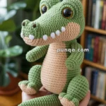 A hand-crocheted stuffed alligator with large eyes, light green body, and a beige belly, held in someone's hands in a cozy room setting with a bookshelf and plants in the background.