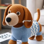 A crocheted dog toy with a brown body, large eyes, and a blue sweater stands on an open magazine on a table, with a plant and chair in the background.